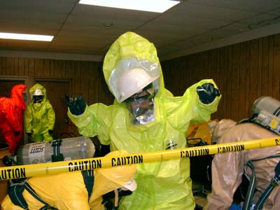A decon team in Level B suits are decontaminating a member of Entry Team 1 after they have left the Hot Zone.